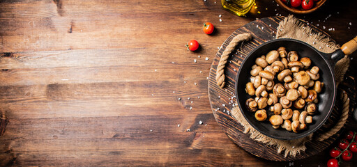 Frying pan with fried mushrooms on a wooden tray. 