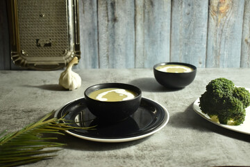 Selective focus picture of Broccoli Soup in a black bowl with broccoli on plate