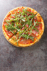 Pizza with prosciutto ham, cheese, tomato sauce and fresh arugula close-up on a wooden board on the table. Vertical top view from above