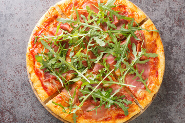 Classic Italian Pizza Prosciutto with tomato sauce, mozzarella, ham, arugula close-up on a wooden board on the table. Horizontal top view from above