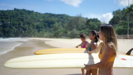4K Group of Asian woman surfer in swimwear holding surfboard walking from the ocean on tropical beach in sunny day. Girl friends enjoy outdoor activity lifestyle water sport surfing on summer vacation