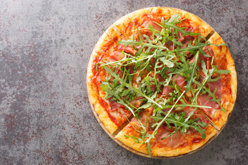 Hot pizza with prosciutto and arugula close-up on a wooden board on the table. Horizontal top view from above