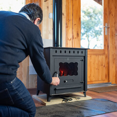Man opening the door of a rustic cast iron stove to light the fire.