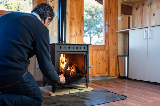 Man Stoking The Fire In A Rustic Cast Iron Fireplace To Heat The House In Winter