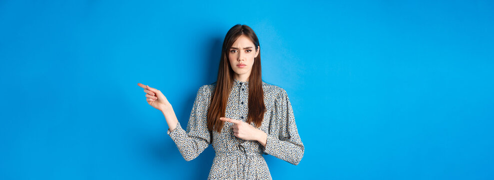 Angry Frowning Woman Pointing Fingers Right And Condemn Person, Feeling Disapointed, Standing In Dress On Blue Background