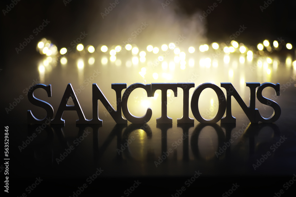 Wall mural word sanctions made of wooden block letters with dramatic lighting and smoke