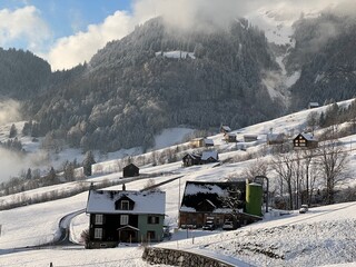 Old traditional swiss rural architecture and alpine livestock farms in the winter ambience over the Lake Walen or Lake Walenstadt (Walensee) and in the Swiss Alps, Amden - Switzerland / Schweiz