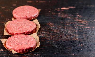 Raw burger on paper. On a rustic dark background.