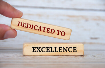 Dedicated to excellence text on wooden blocks with wooden cover background. Business motivation concept
