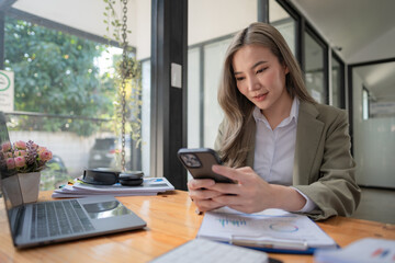 Portrait of an Asian woman sitting at her desk with a laptop and adhesive notes using a mobile phone. Asian businesswoman working in a modern office.