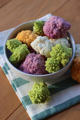 Various sort of cauliflower in a bowl on wooden table. Purple, yellow, white and green color...