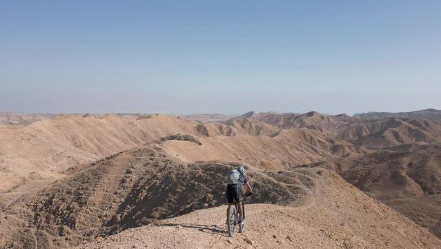 Mountain Biking Downhill steep narrow rocky ridges with scenery in the wild alone near the Dead Sea lake and Arad Mountains in the Negev Desert, Israel with bright blue sky Aerial Active Track Follow 