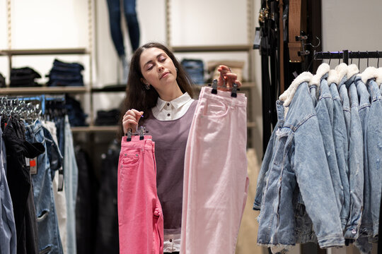 Second hand. Pretty young Caucasian woman comparing between two hanger with jeans. Concept of shopping and fashion