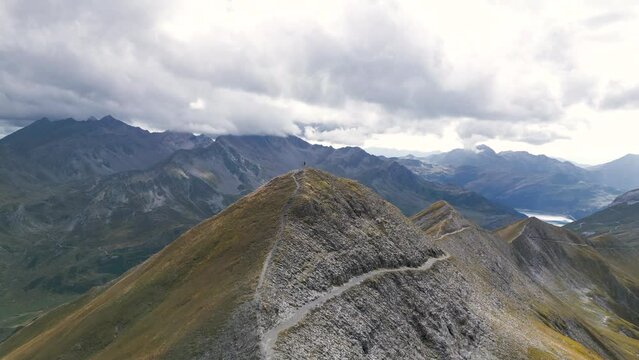 Aerial Epic Man standing on top of a mountain with panoramic view with mountains, lakes and clouds, Drone view, in the French Alps, France, Tour du Mont Blanc, near Refuge Croix du Bonhomme