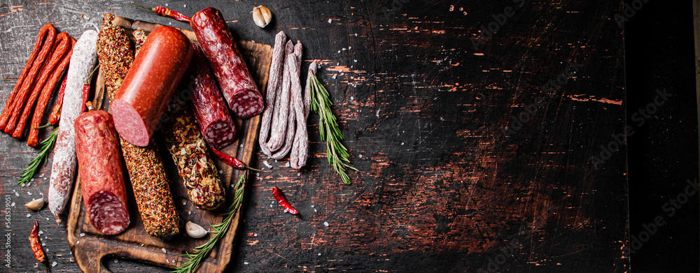 Poster Different types of salami sausage on a cutting board with rosemary. 