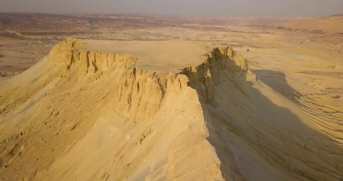 Approaching a flat mountain with cliffs in the desert during a summer sunrise with clear sky, Aerial flying above revealing ridge in Tsin Mountain, Negev Desert, Israel