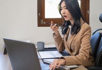 Woman looks at laptop makes order on-line, talks to sales manager on smartphone, discuss purchase,...