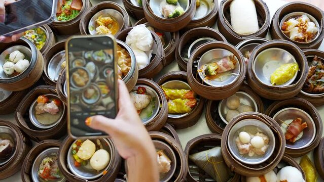 Group of Asian woman hands using mobile phone taking picture Chinese food steamed dumpling in bamboo steamer at restaurant. Girl friends enjoy eating street food and travel together on summer vacation