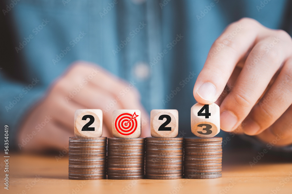 Poster businessman hand flipping wooden block cube from 2023 to 2024 on coins stacking for setup objective 