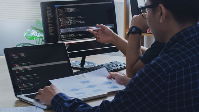 Couple Young programmer writing program code sitting at the workplace with laptop and computer in the office.