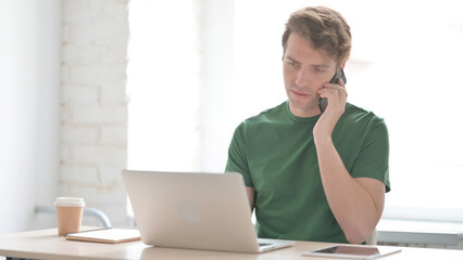 Young Man Talking on Phone while using Laptop