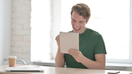 Young Man Celebrating Success on Digital Tablet at Work