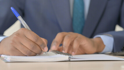 Close Up of Young African Businessman Hand Writing on Notebook