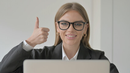 Thumbs Up by Young Businesswoman while using Laptop
