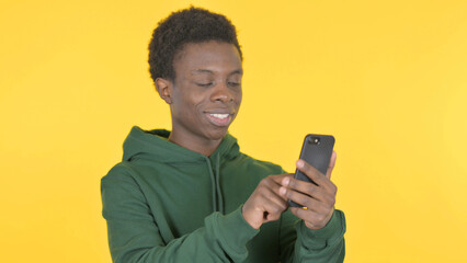 Young African Man Browsing Smartphone on Yellow Background