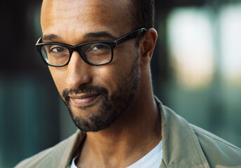 A young unshaven afro american smiling man wearing eyeglasses on the street. Outdoor portrait.