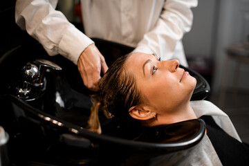 Close-up of female client relaxed on hair washing chair while hairdresser washes her hair