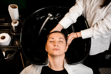 top view on female client relaxed lying on hair washing chair with her eyes closed while...