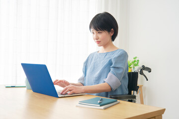 家でパソコンを使う車椅子に乗った障がい者女性