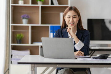 Professional Asian female accountant focusing on her sales account Cropped view of calculator in accounting firm working on financial auditing and budgeting using laptop in online meeting