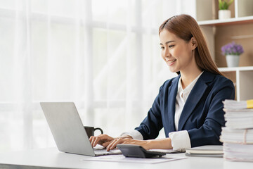 Professional Asian female accountant focusing on her sales account Cropped view of calculator in accounting firm working on financial auditing and budgeting using laptop in online meeting