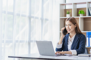 Asian businesswoman accountant using smartphone to chat with clients in accounting firm working on financial auditing and budgeting using calculator and laptop.