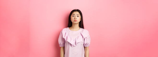 Sad whining asian girl pouting and frowning, looking upset about something unfair, complaining,...