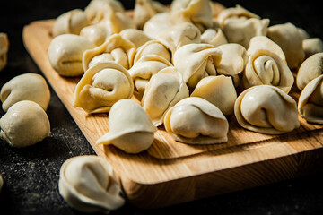Raw homemade dumplings on a wooden cutting board. 