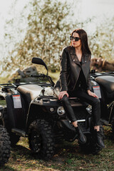 Fototapeta na wymiar sexy girl with long dark hair on quad bike; dressed in black leather clothes; sunglasses on the eyes; posing on a quad bike
