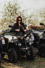 Plakat sexy girl with long dark hair on quad bike; dressed in black leather clothes; sunglasses on the eyes; posing on a quad bike
