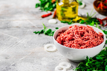 Minced meat in a bowl on a table with parsley and onion rings. 