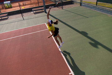 Professional equipped female tennis player beating hard the tennis ball with racquet. Top view.