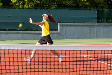 Professional equipped female tennis player beating hard the tennis ball with racquet.