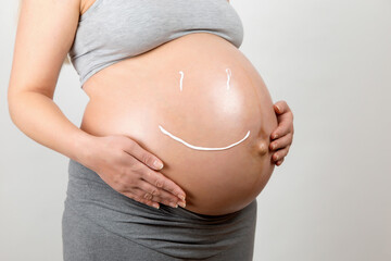 Cream on the stomach of a pregnant girl in the form of a smiley. Skin care, prevention of stretch marks.