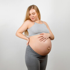 A pregnant girl, on a gray background. Big stomach, back pain.