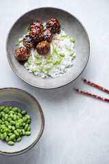 Plate with teriyaki meatballs and white rice, top view on a light-grey granite background, vertical shot with space