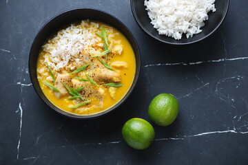 Yellow curry with fish and white rice on a black marble background, horizontal shot, above view