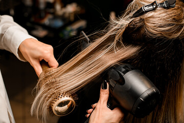 Close-up of hairdo making process. Hairdresser puts female hair with dryer and comb - Powered by Adobe