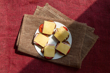 Top view of several self-made sandwiches on white plate lie on rustic fabric background