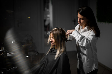 Great view on professional stylist curling hair of woman with clipless iron at salon